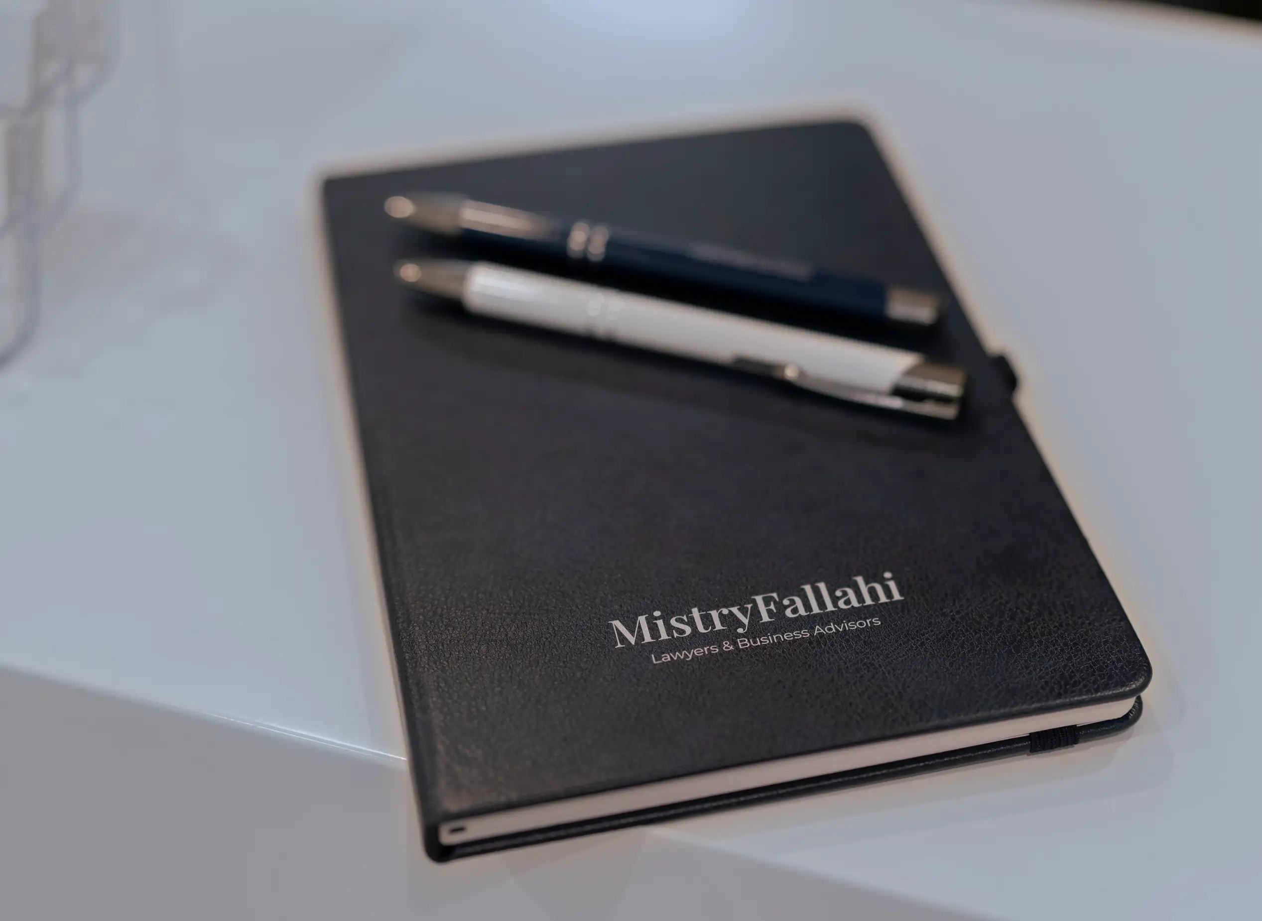A navy MistryFallahi notebook with a navy pen and a white pen resting on it