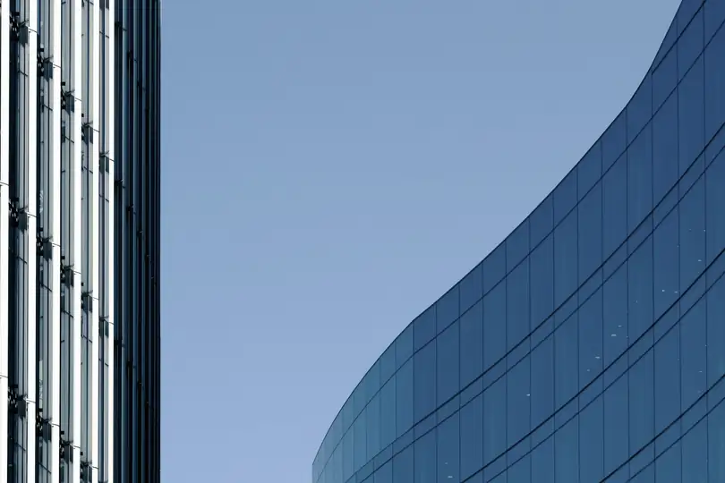A curved blue glass wall beside a tall tower