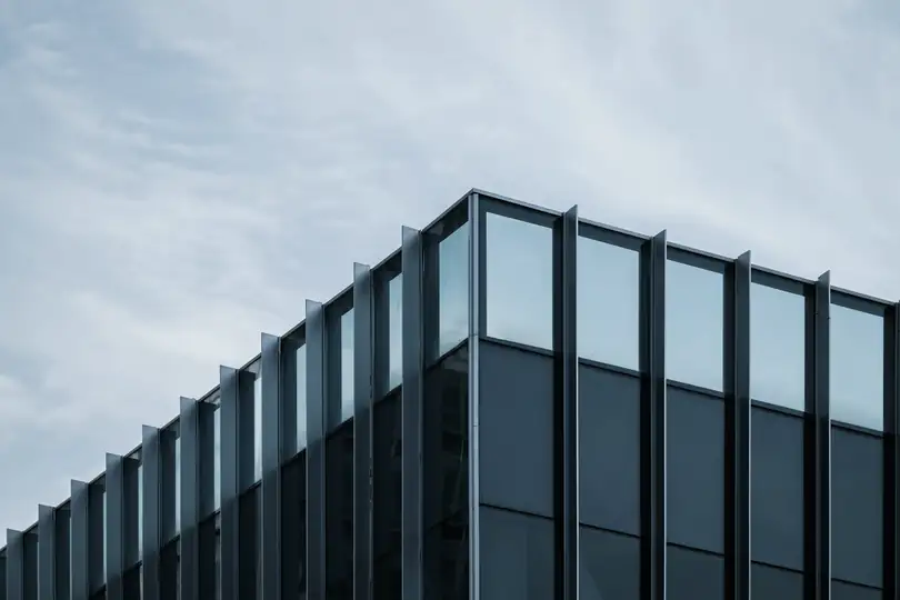 The upper floors of a dark glass office building under cloud