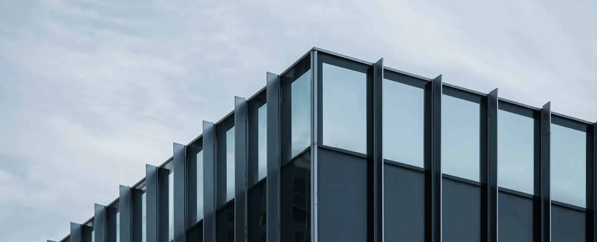 The upper floors of a dark glass office building under cloud