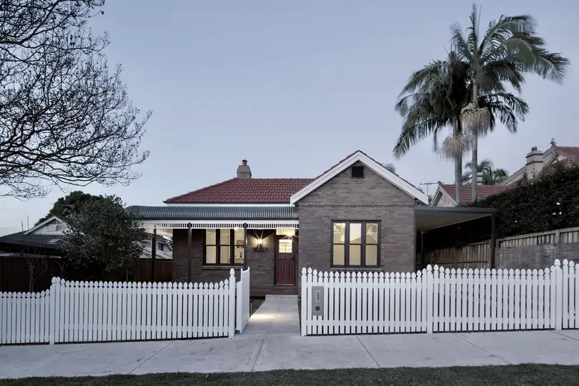 A brick house with a tiled roof behind a white fence