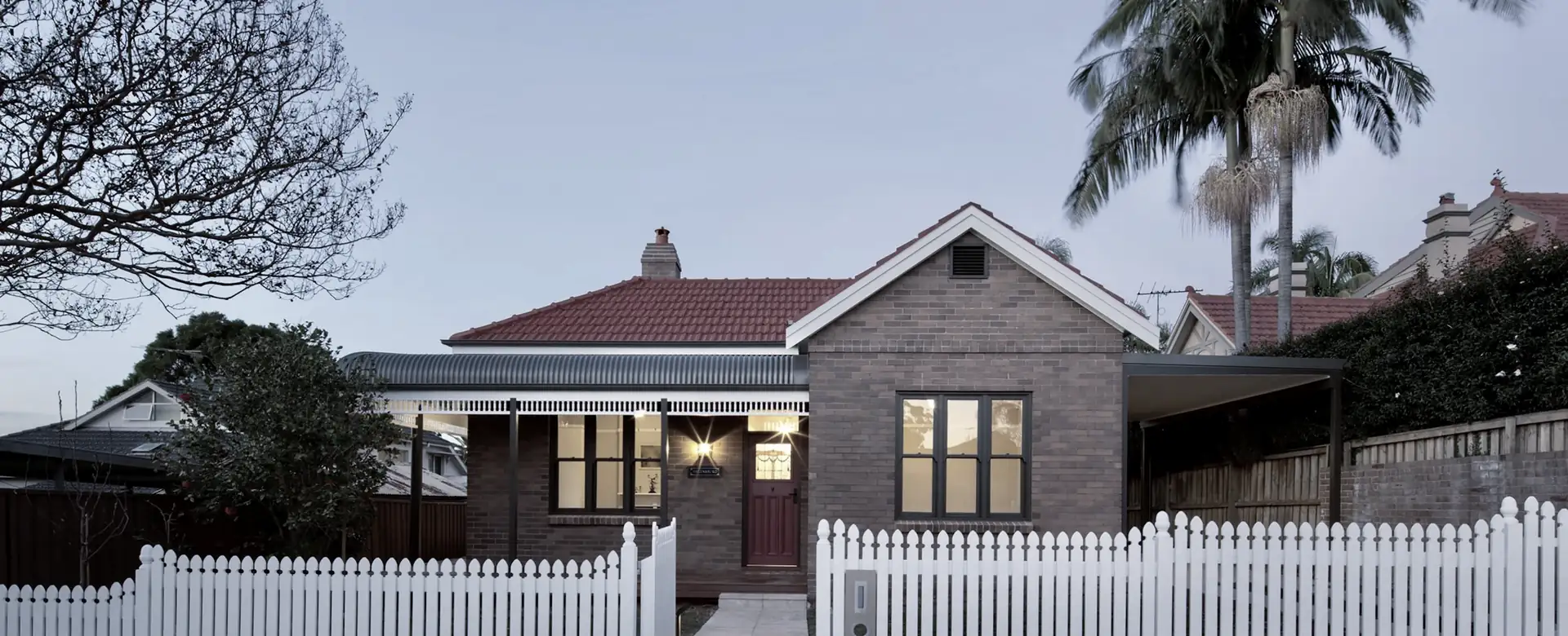 A brick house with a tiled roof behind a white fence