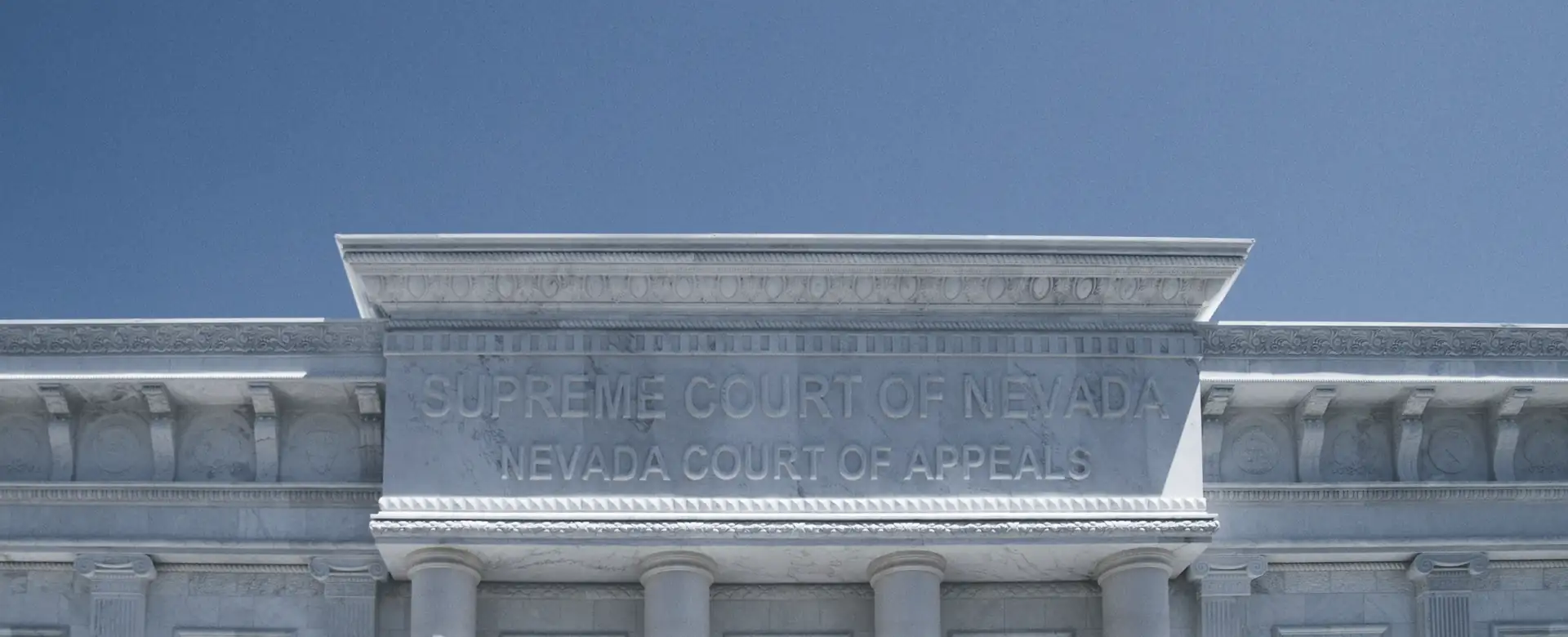 The top of a white classical building against a blue sky