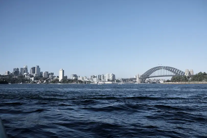 A city skyline and a steel arch bridge across blue water
