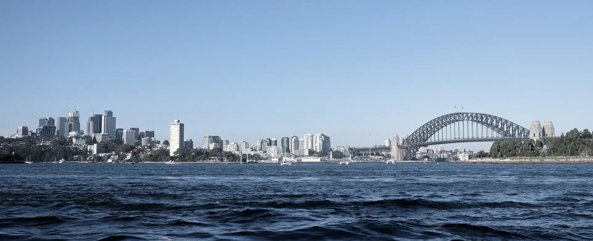 A city skyline and a steel arch bridge across blue water